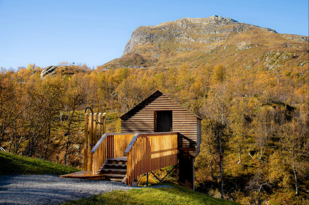 Wooden cabin in an autumn forest valley with distant mountains and clear blue sky