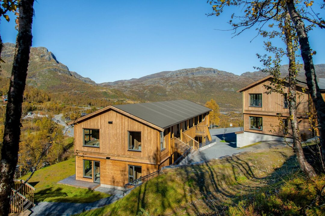 Wooden cabins in a mountain valley surrounded by trees under a clear blue sky