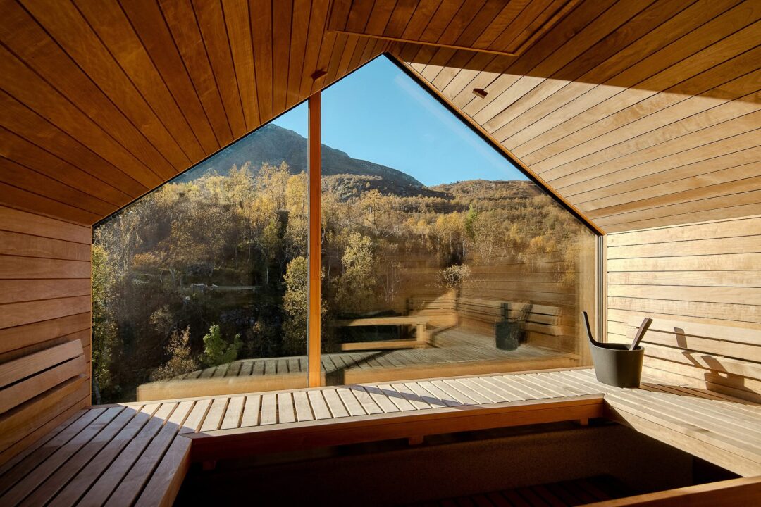 Wooden sauna cabin interior with benches and a view of forested mountains through a triangular window