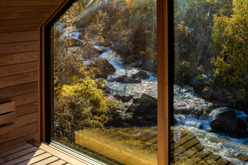 View from a wooden cabin window over a fast rocky river and autumn forest in the countryside