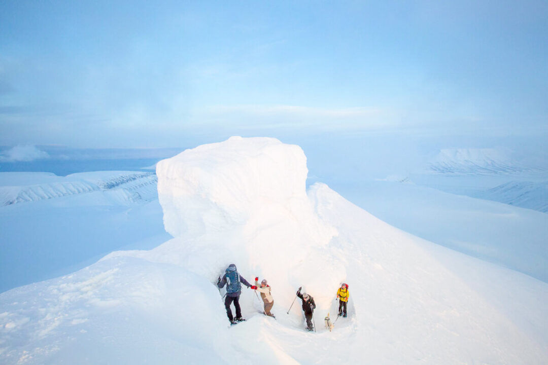 Women snowmobiling across snowy Svalbard terrain with distant icebergs and mountains in clear daylight