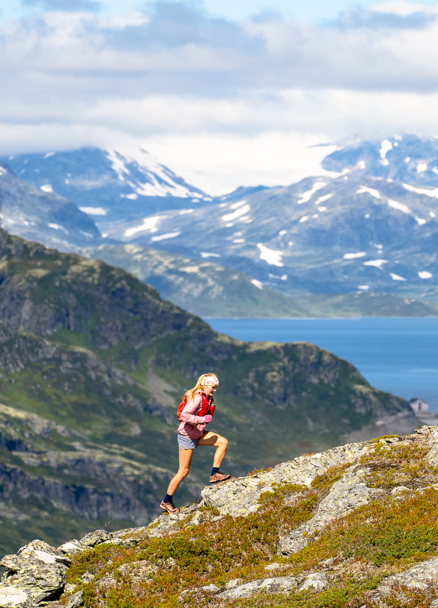 Woman hiking on a rocky ridge overlooking mountains and fjord in Jotunheimen National Park