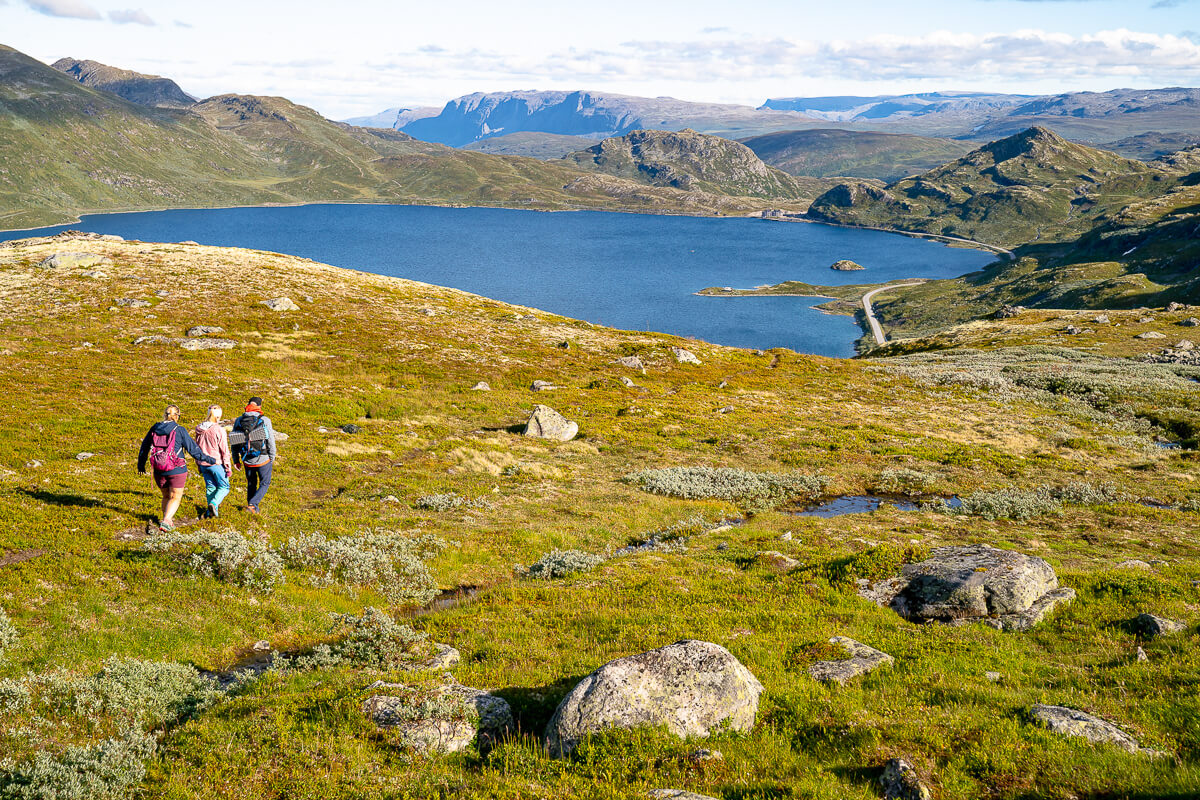 Women hiking a mountain trail overlooking a lake and snow-capped peaks in Norway