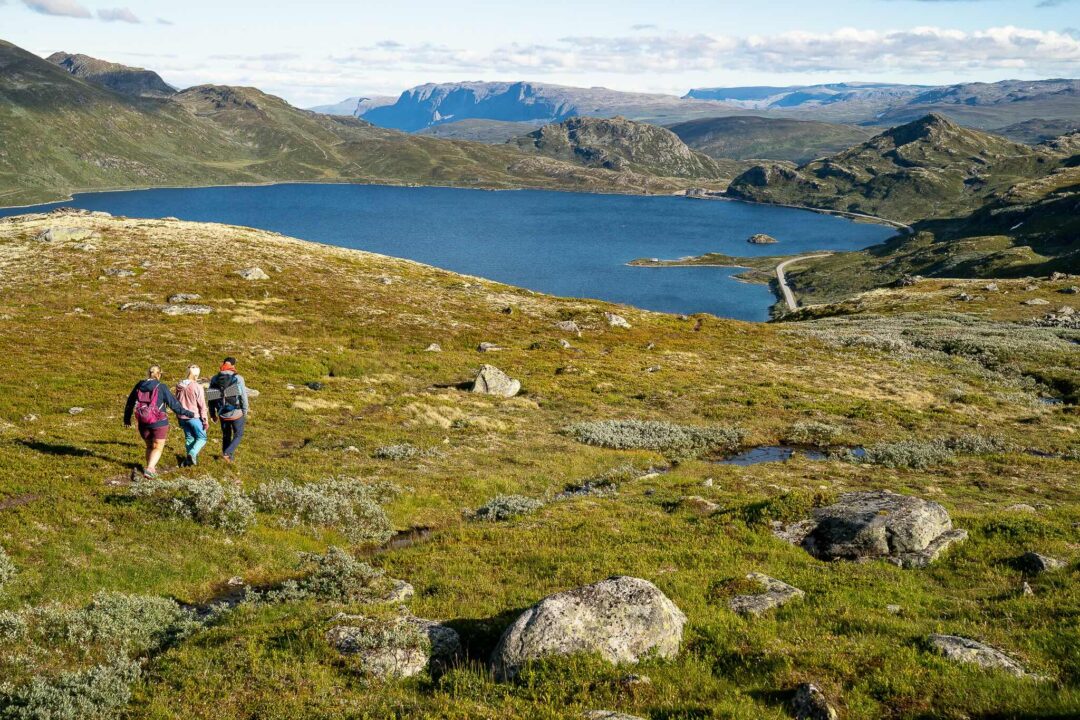 Women hiking along a mountain trail above a glacial lake and valley landscape