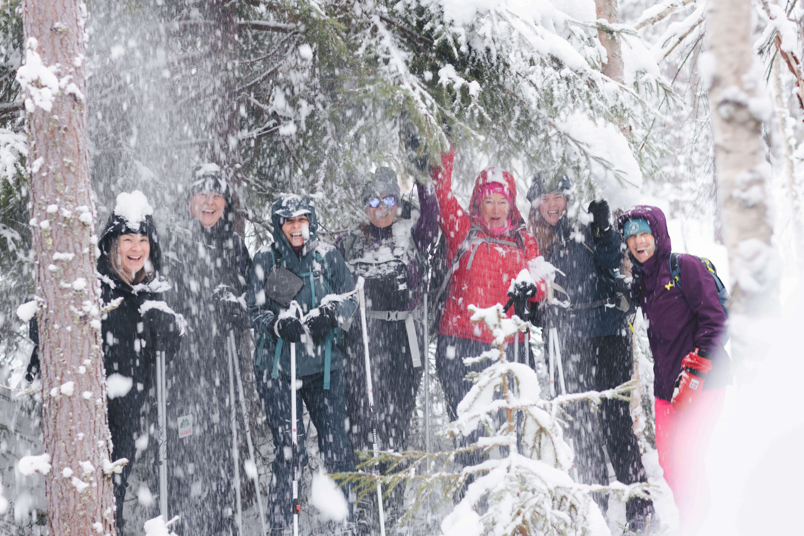 Women in winter clothing smiling on skis in a snowy forest with heavy snowfall