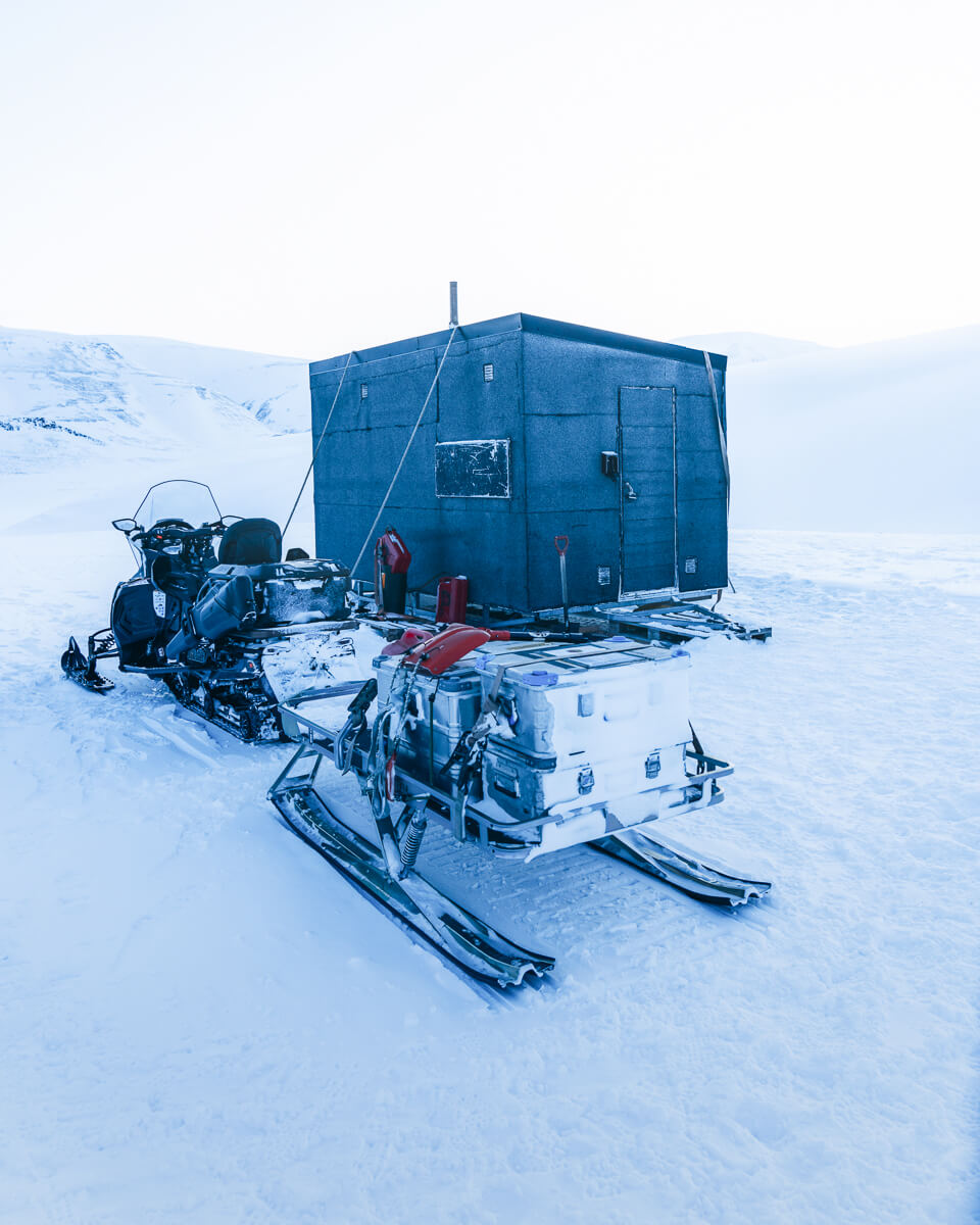 Snowmobiles parked beside a blue shelter in a snowy Arctic landscape
