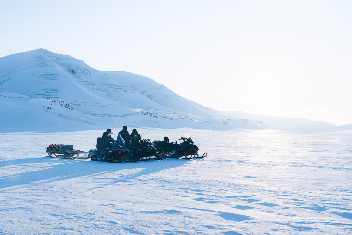 Women snowmobilers riding across snowy tundra with mountains in Svalbard, Arctic landscape
