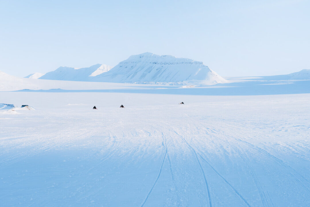 Snowmobiling tracks across snowy terrain towards distant mountains in Svalbard