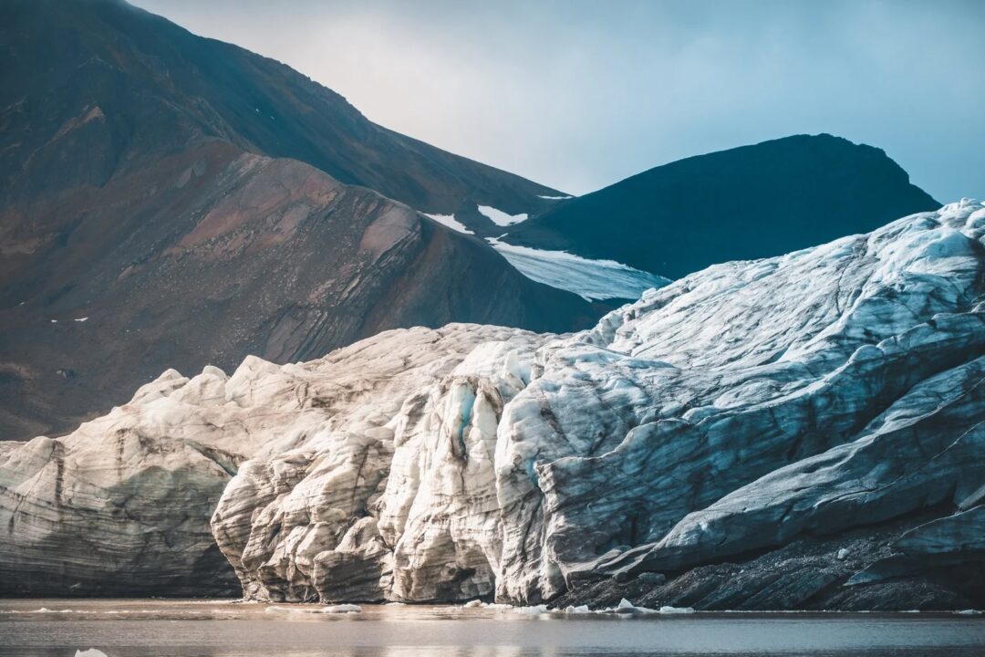 Svalbard Arctic wilderness glacier with blue ice flowing into the sea beneath dark mountain peaks