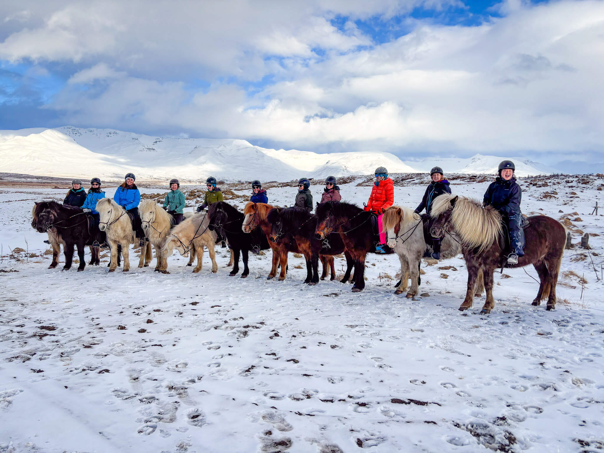 Women standing with horses in a snowy landscape with mountains, on a winter ride