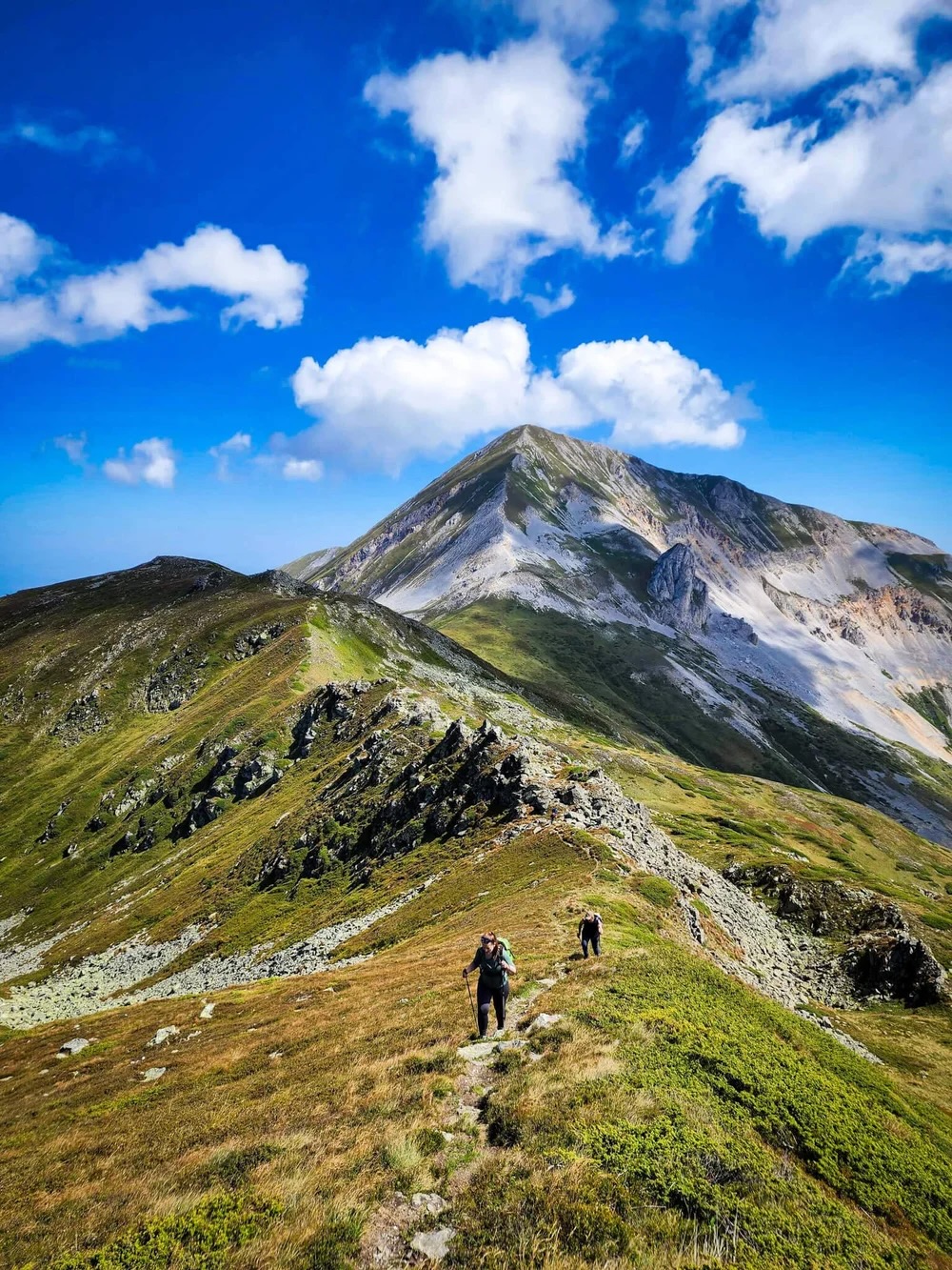 Hikers on a mountain hiking trail with a rocky peak and blue sky with clouds