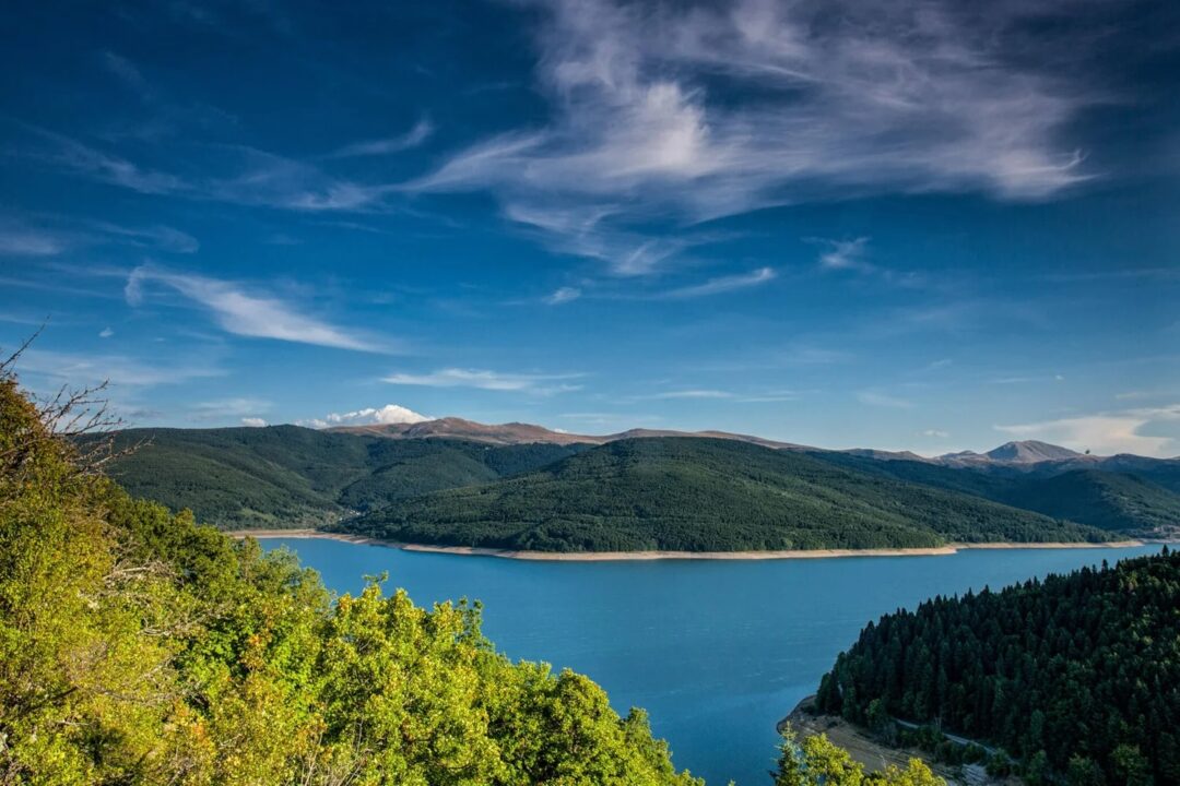 Scenic mountain lake and forest landscape under a blue sky, with distant peaks on the horizon