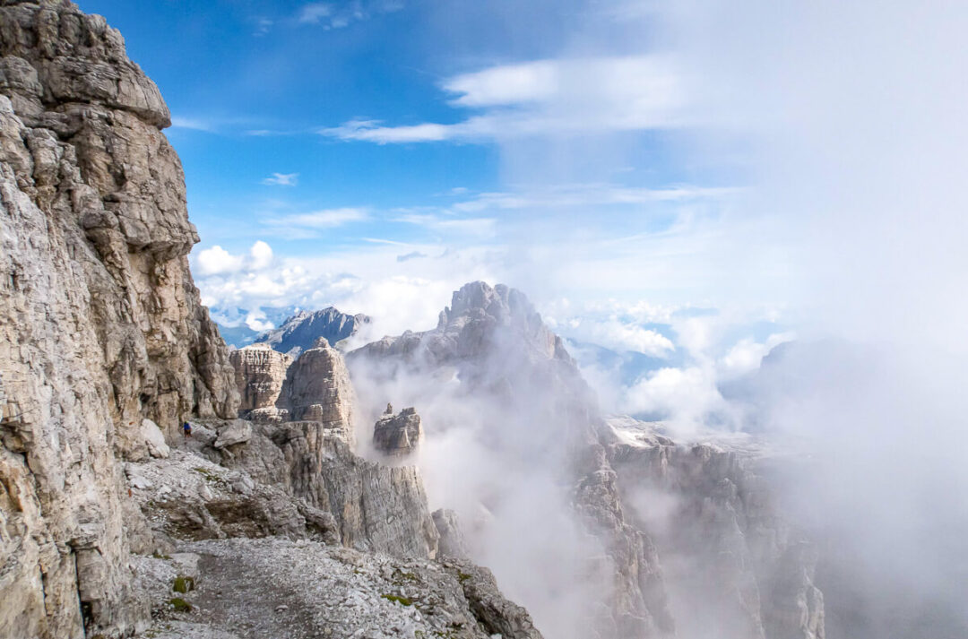 Via ferrata trail along a rocky cliff in the Dolomites, with dramatic mountain peaks and clouds below