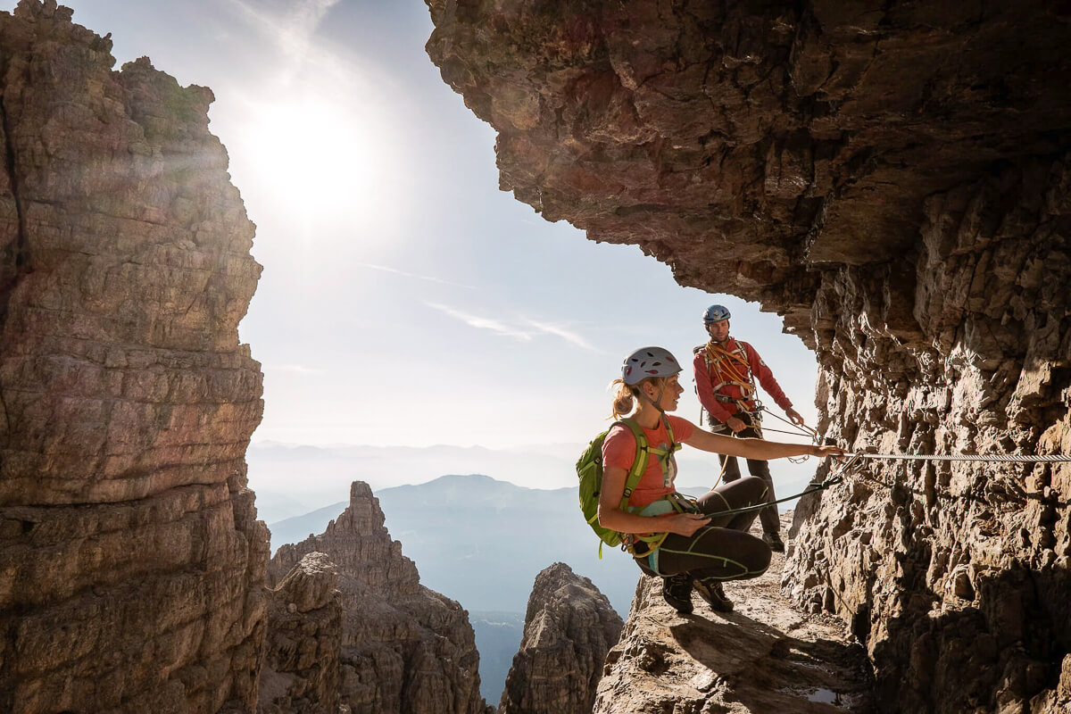 Woman and guide on a via ferrata route in the Dolomites, rocky cliff walkway with cable handrail