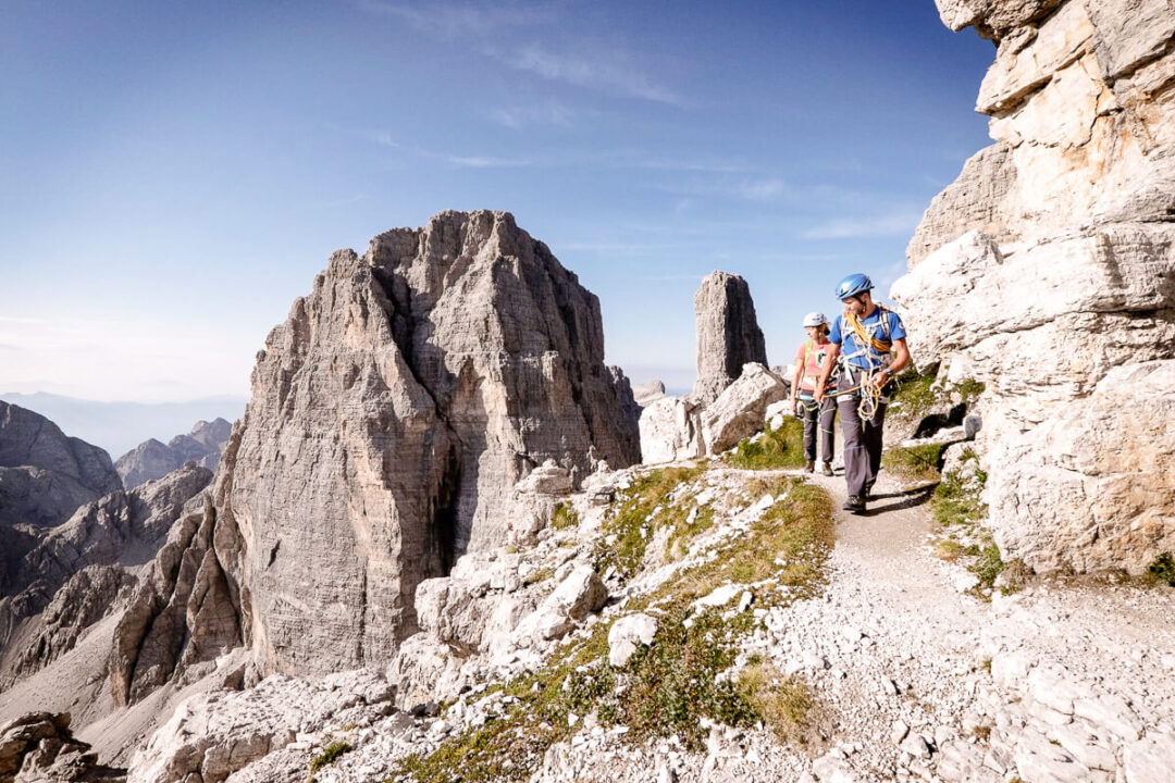 Women hiking a via ferrata trail along rocky cliffs in the Dolomites, Europe, wearing helmets and harnesses