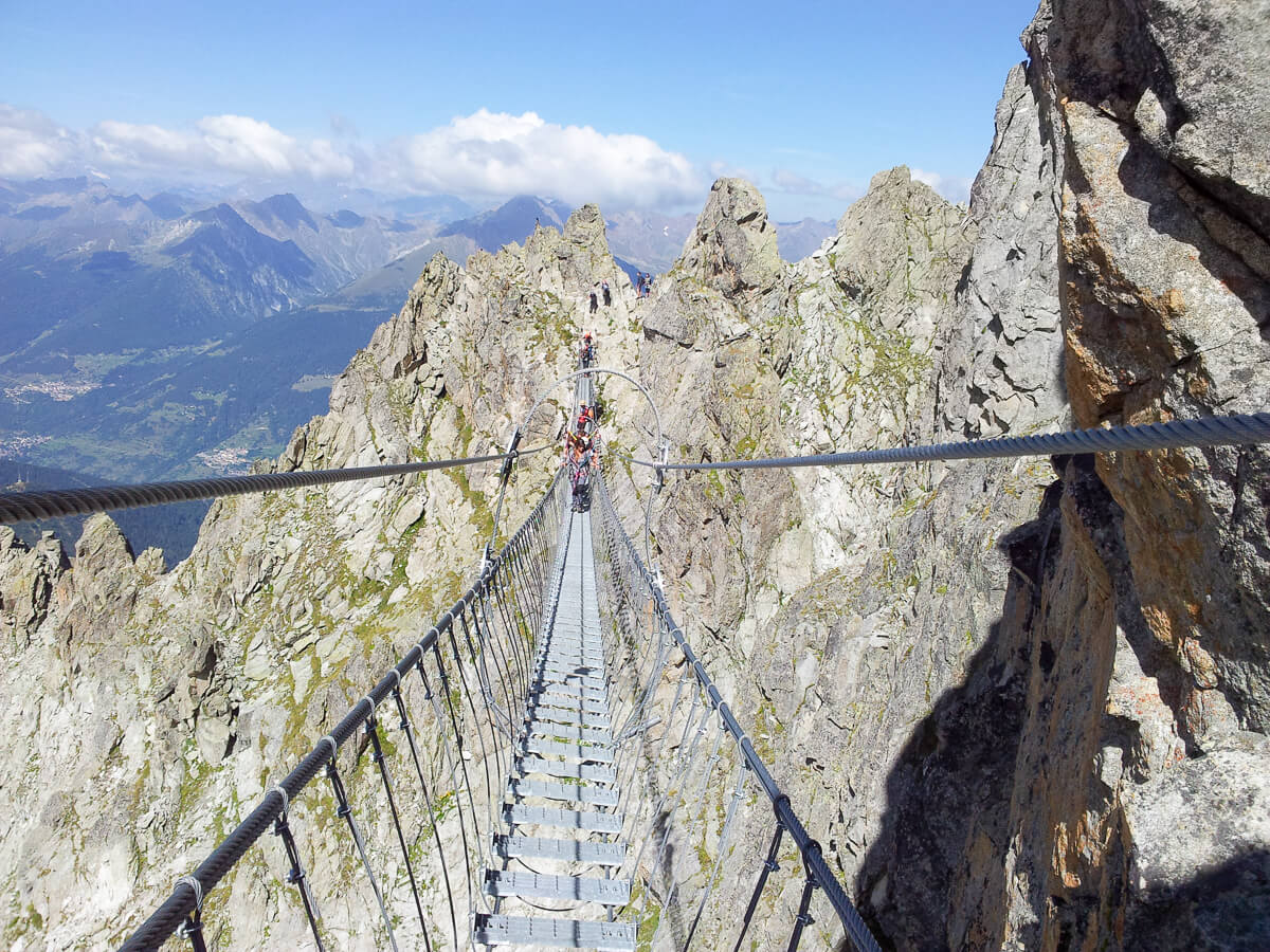 Suspension bridge across jagged peaks in the Dolomites, Italy, with women walking over the mountains