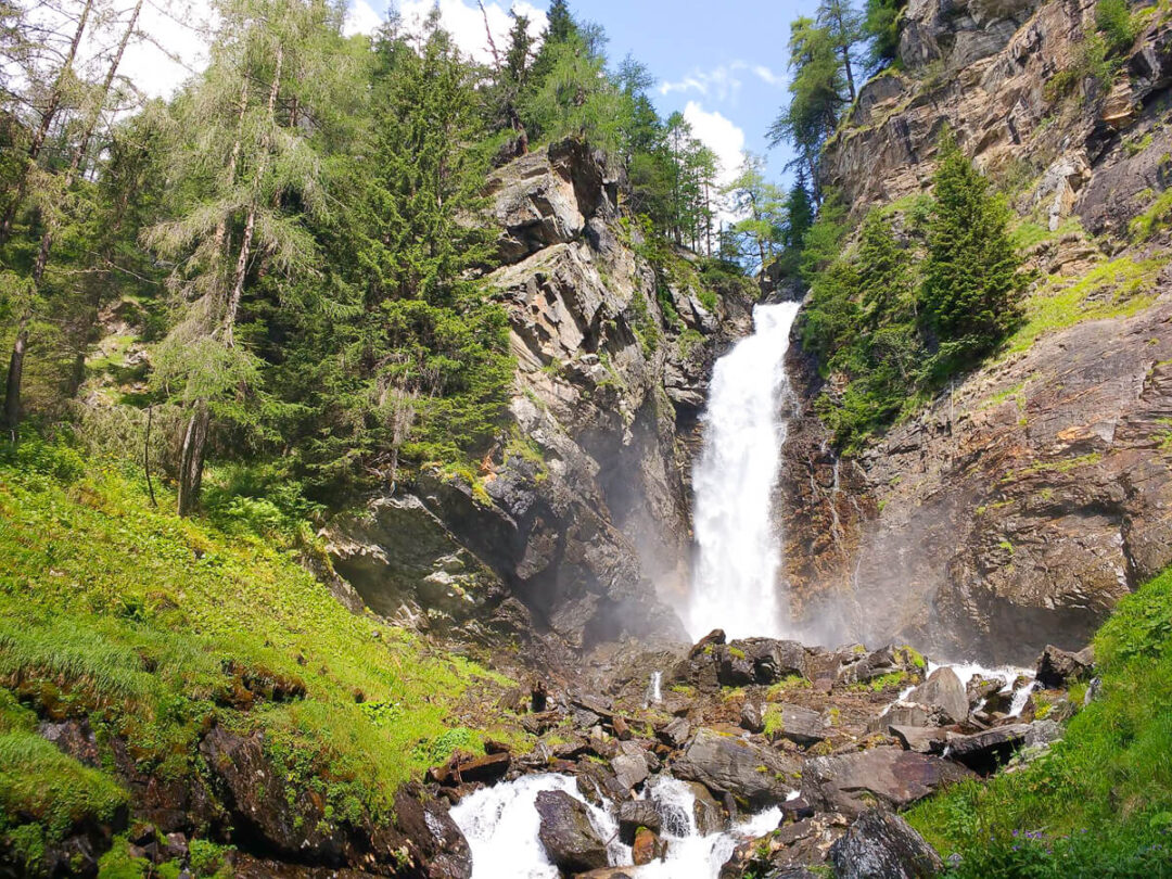 Dolomites waterfall in Italy, cascading down rocky cliffs through a green alpine valley