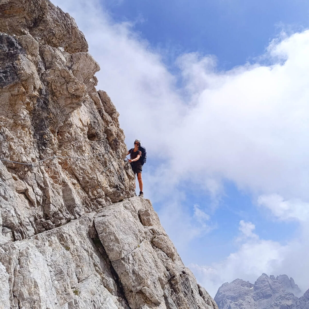 Woman standing on a rocky cliff face in the Dolomites under a cloudy blue sky