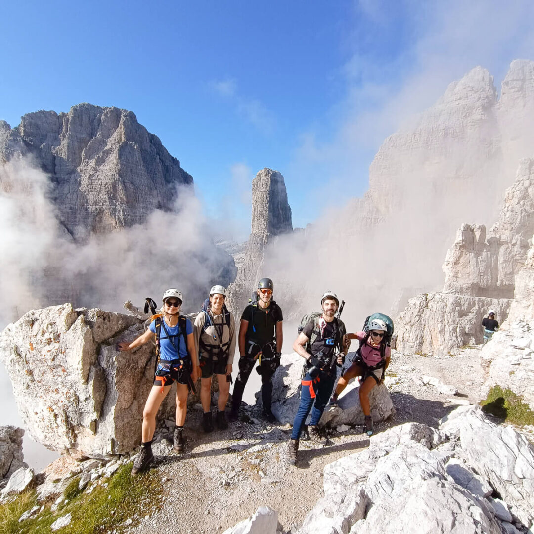 Women on via ferrata in the Dolomites, with rocky peaks and clouds in the background