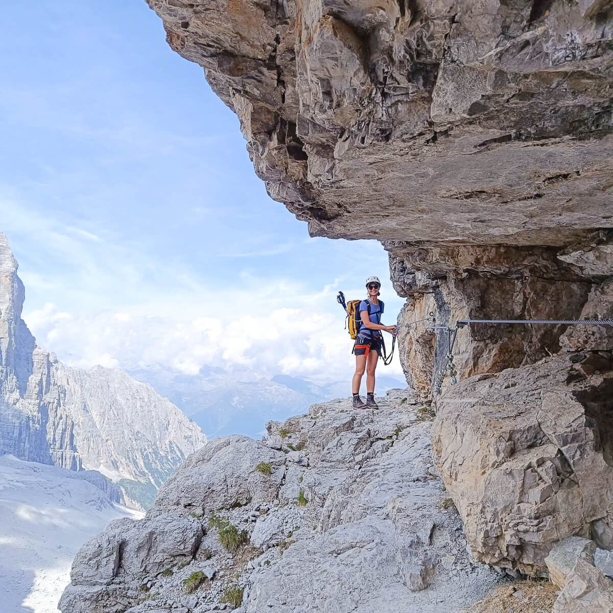 Woman on via ferrata route on rocky cliff in the Dolomites, wearing harness and via ferrata lanyards