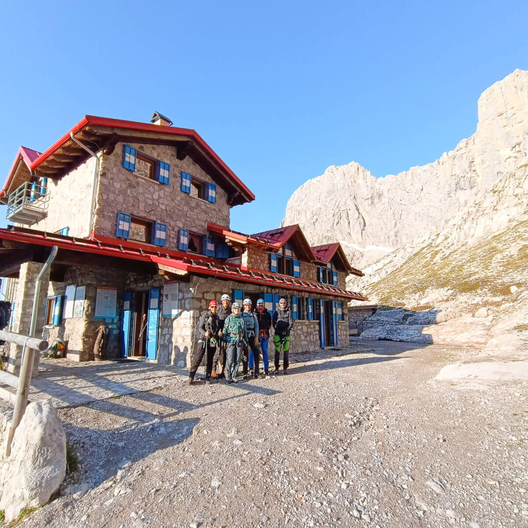 Women hikers stand in front of a mountain hut in the Dolomites, ready for a via ferrata hut-to-hut trip
