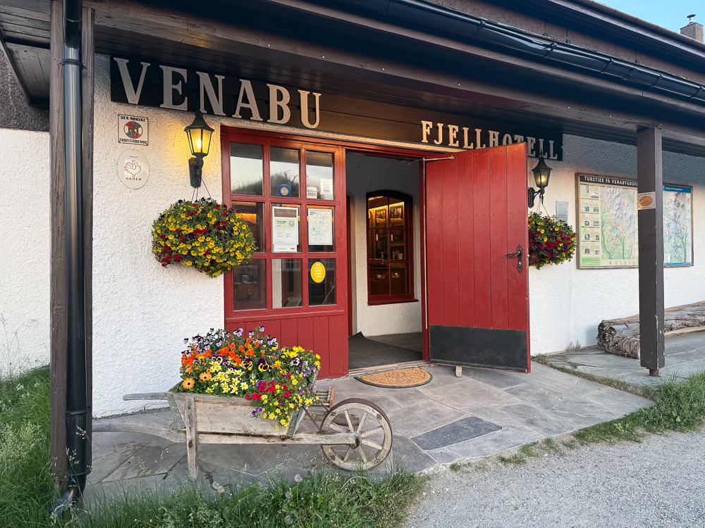 Venabu Fjellhotel entrance with “VENABU” sign and red door, flowers and bicycle outside