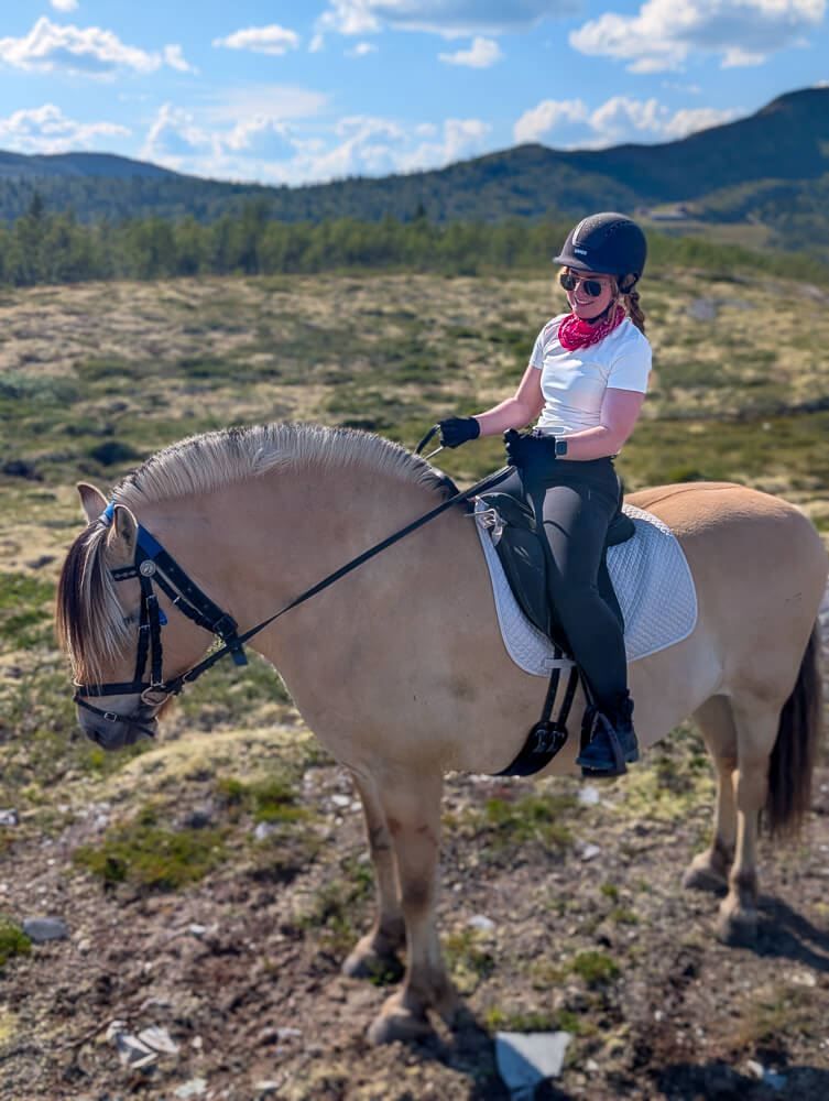 Woman horseback riding in Norway’s mountainous countryside under a blue sky