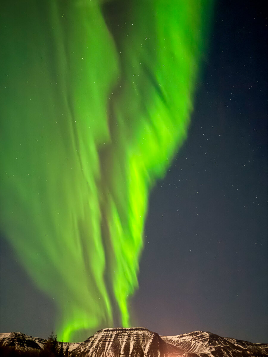 Northern lights (aurora borealis) over dark mountains at night in Iceland