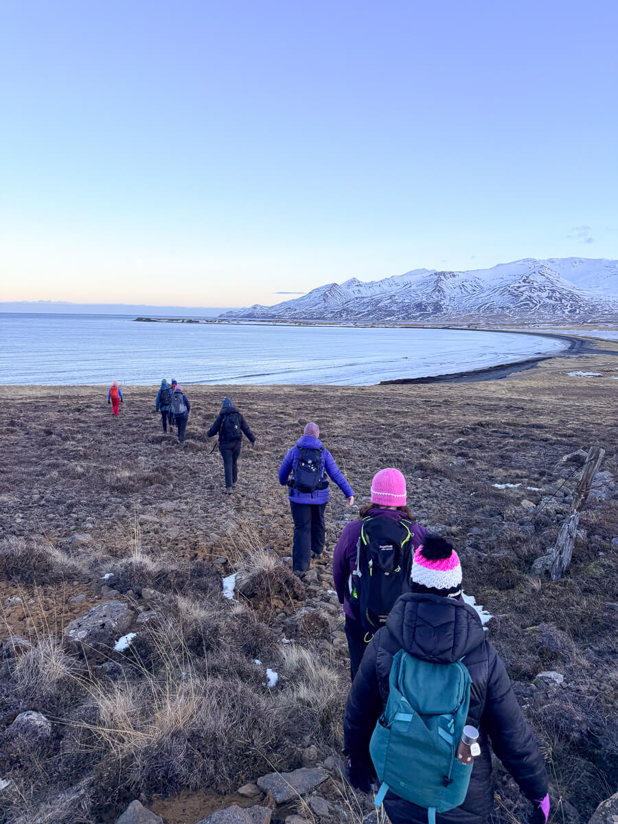 Women hiking along a snowy coastal path with mountains in North Iceland during winter