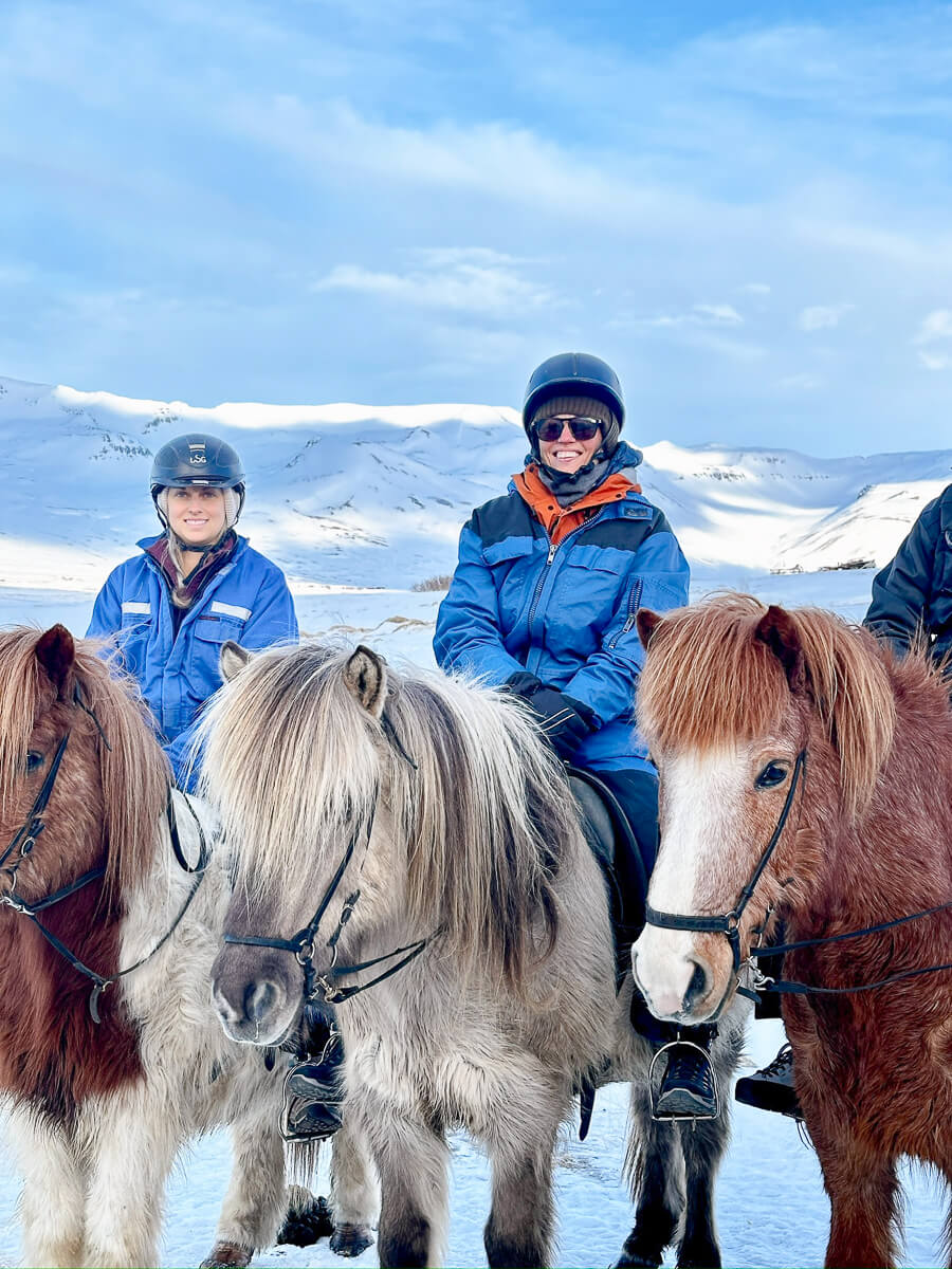 Women in winter jackets with saddled horses during horse riding in snowy mountains