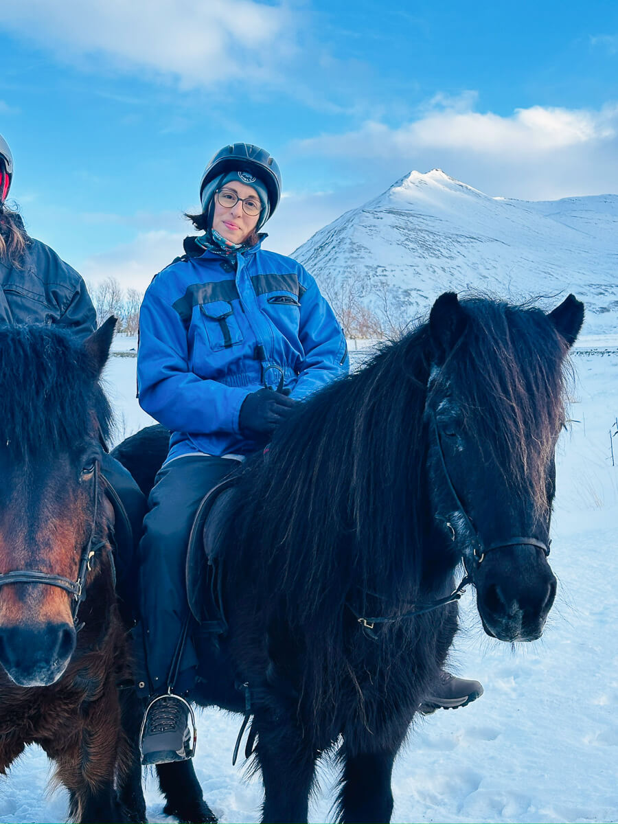 Woman riding a horse in snowy winter landscape with mountains in North Iceland