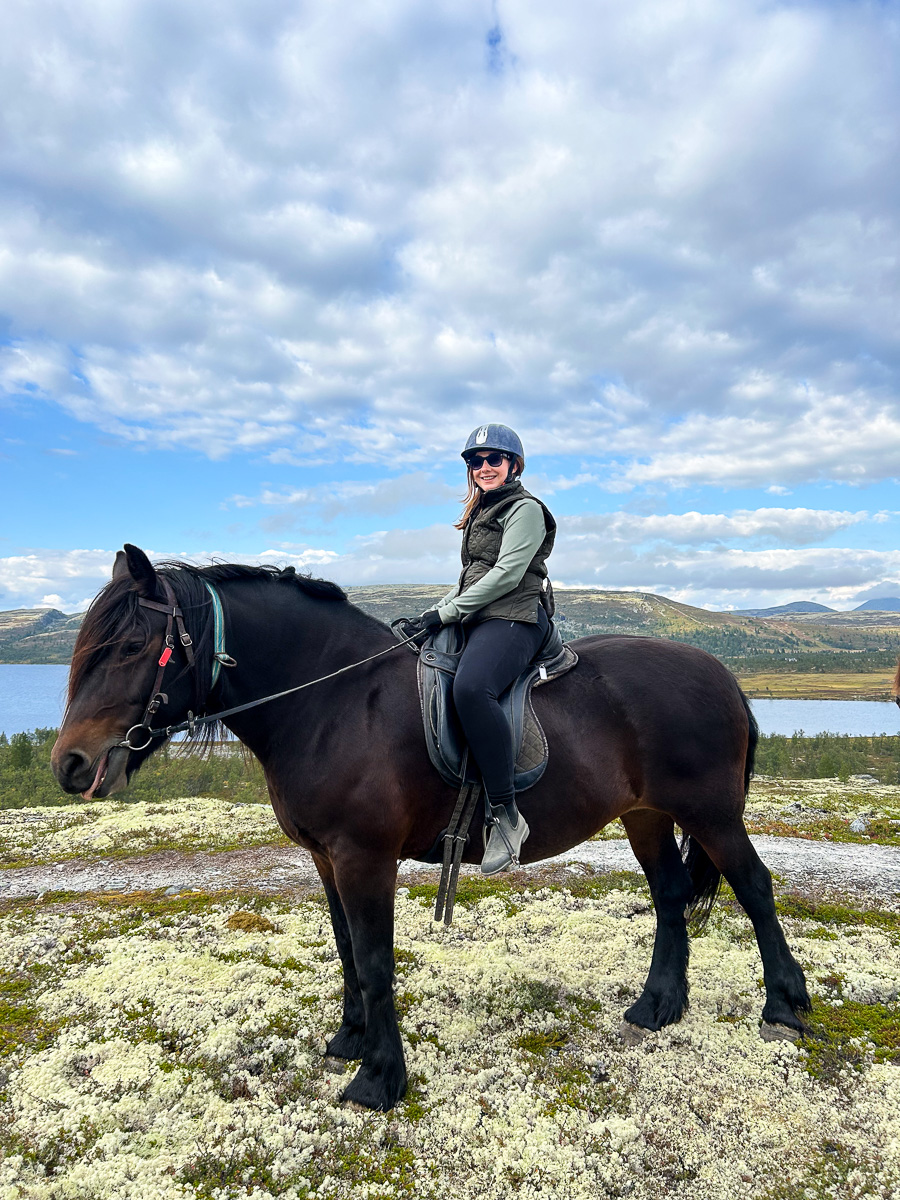 Woman horseback riding in Norway with mountains and lake landscape in the background