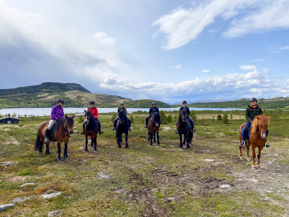 Women on horseback in Norway, riding outdoors with mountains and green hills in the background