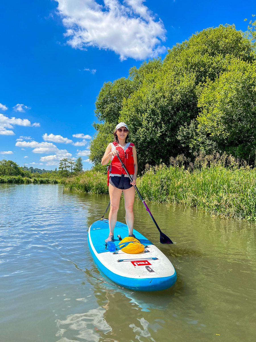 Woman paddling a stand-up paddleboard on a calm river near trees under a blue sky