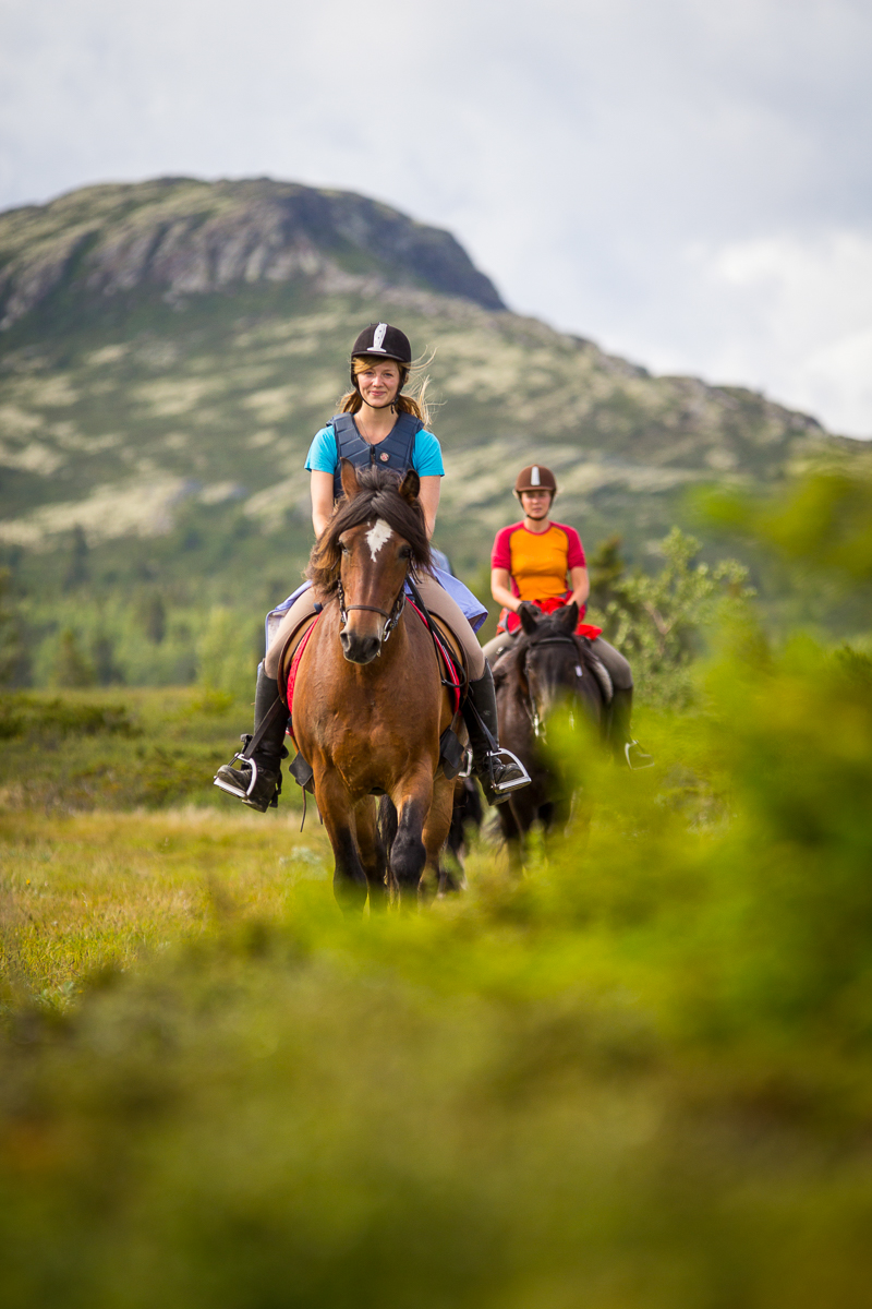 Two women riding horses through a green mountain valley on a countryside adventure holiday in Europe