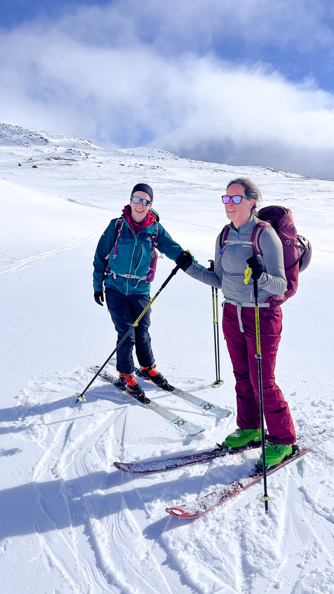 Women ski touring with backpacks on snowy mountain slopes under a blue sky