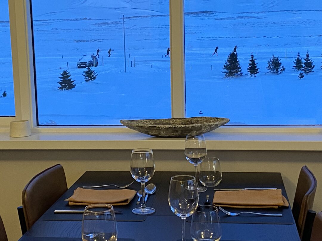 Dining table by a window with view of snowy ski slopes in North Iceland, winter skiing activity outdoors.