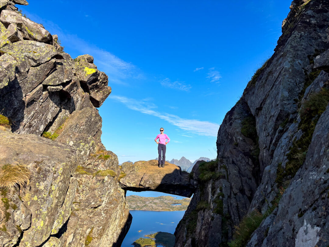 Woman hiking on rocky coastal cliffs above a calm fjord under a clear blue sky