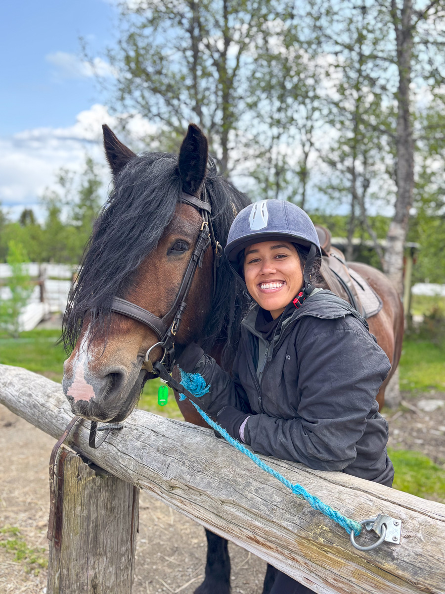 Smiling woman in a riding helmet with a horse outdoors on a wooden rail