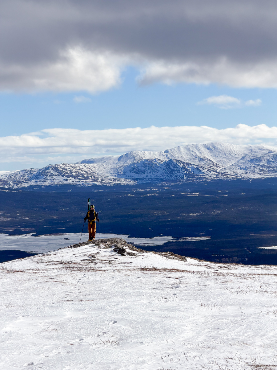 Woman ski touring on a snowy ridge overlooking Swedish mountains under a cloudy sky