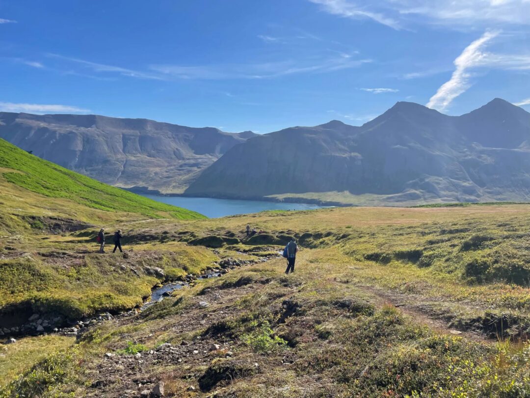 Women hiking across Icelandic valley with mountains and a lake in the distance