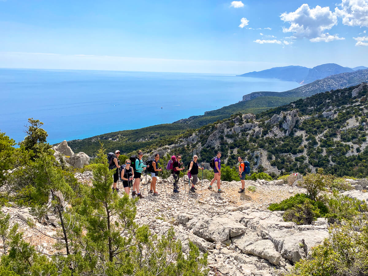 Women hiking on a rocky trail with sea and cliffs, Sardinia east coast