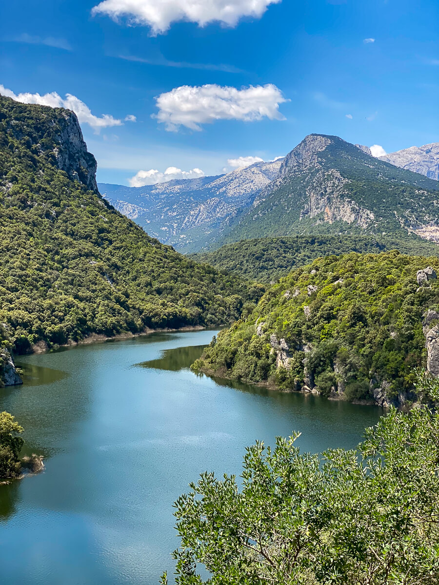 Scenic hike along Sardinia’s east coast overlooking a calm river and forested mountains under blue sky