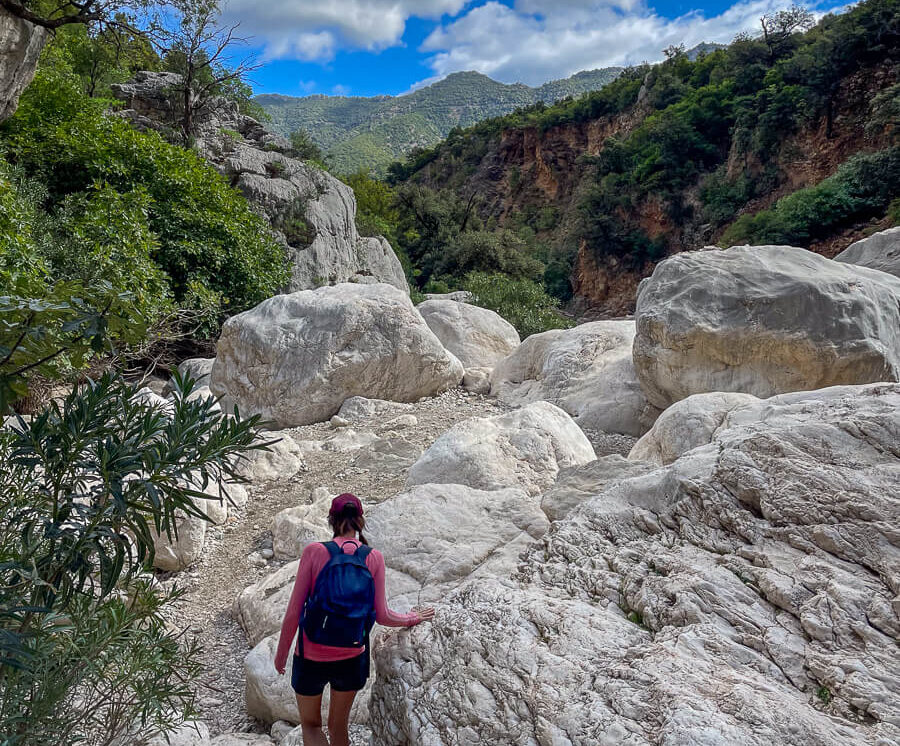 Woman hiking over a rocky trail in East Sardinia mountains, surrounded by forest.