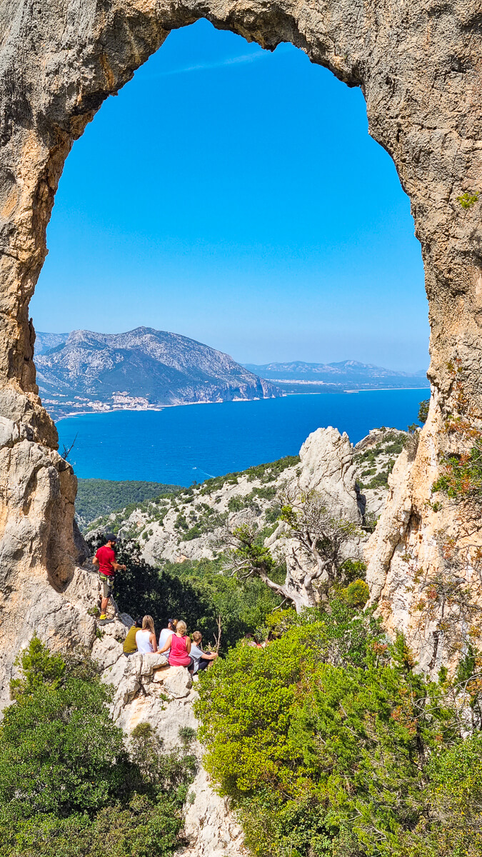 Women hikers at a rocky arch overlooking the blue sea on Sardinia’s east coast, during a scenic hike.