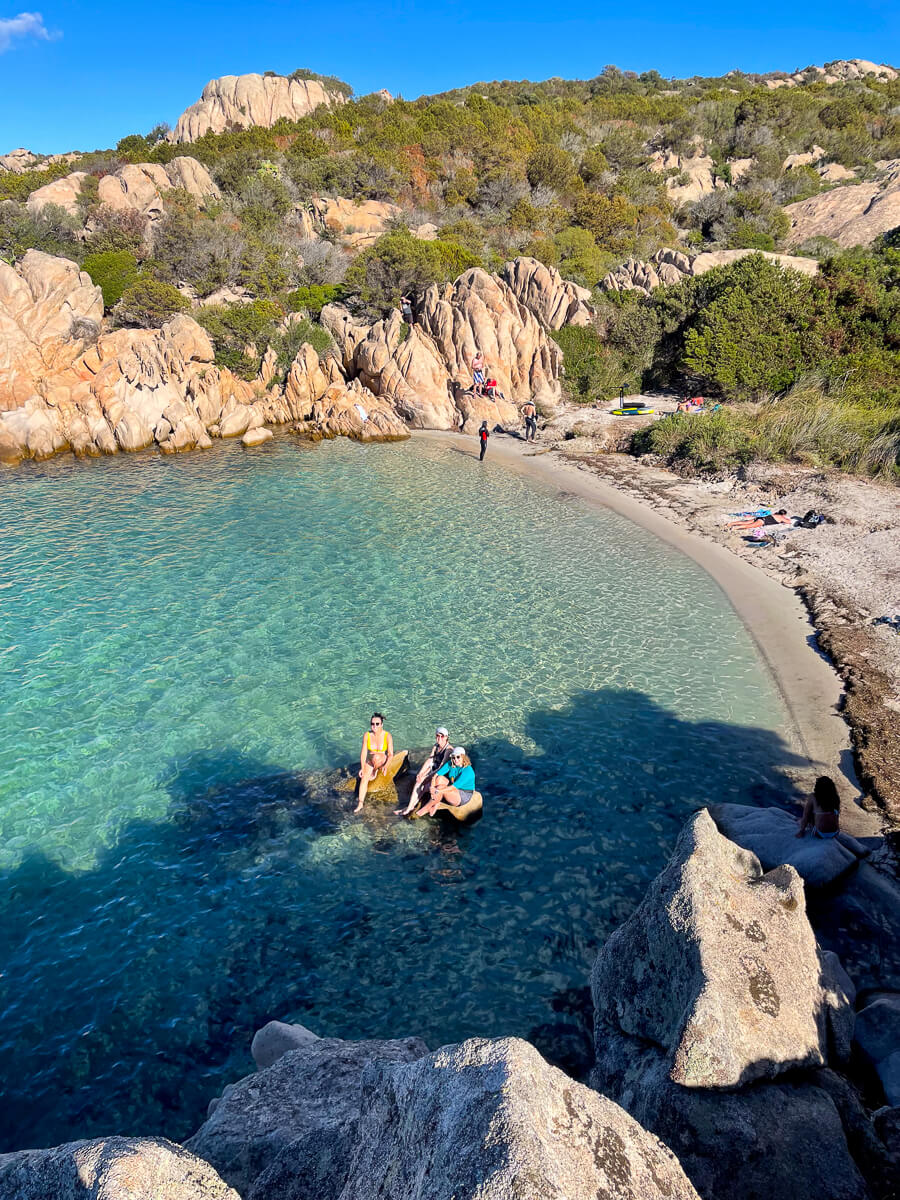 Women kayaking near a rocky beach in East Sardinia, with clear turquoise sea and hills in view