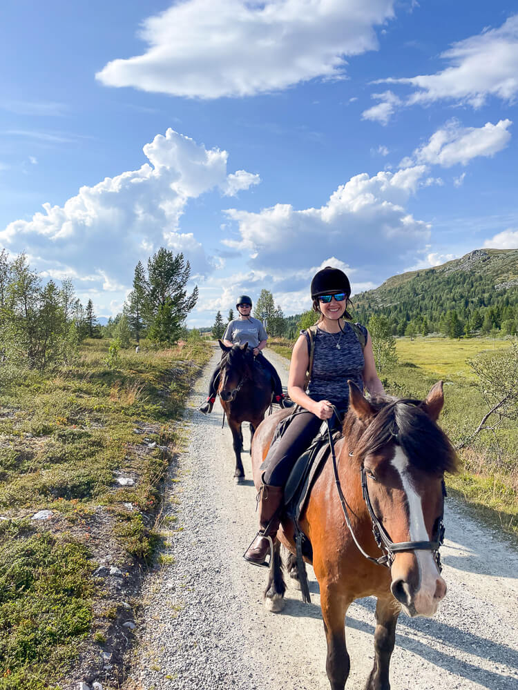 Women horse riding along a gravel path through green valleys and mountains in the countryside