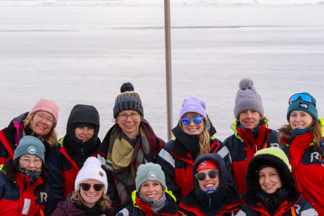 Women in winter jackets and hats smiling outdoors in snowy landscape