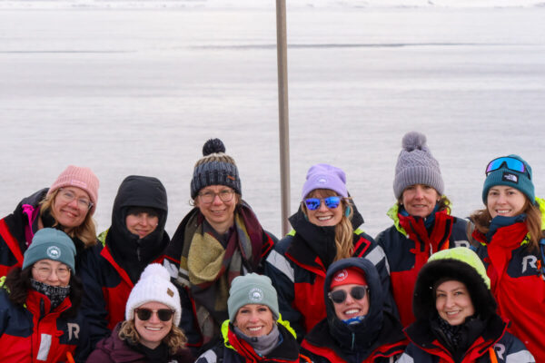 Women in winter jackets and hats smiling outdoors in snowy landscape