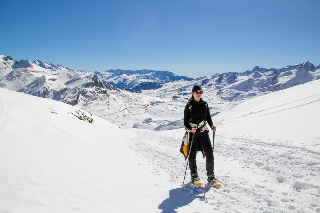 Women snowshoeing in a snowy Pyrenees mountain landscape with ski tracks and peaks under a clear blue sky
